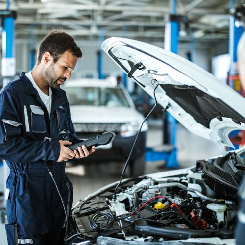 Young mechanic analyzing car's performance with diagnostic tool in a workshop.